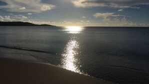 Una playa con mar tranquilo, cielo despejado y el sol reflejado en el agua.