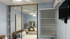 Un dormitorio con cama, mesita de noche, espejo, ventilador de techo y aire acondicionado de pared.