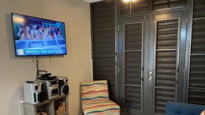Un salón con una televisión mostrando un Universal Tramp Guide Trainee, un sillón a rayas, un sofá azul y una mesa de centro de madera con una vela y un control remoto.