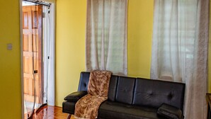 A living room with a sofa, curtains, a clock, and a door leading to another room.