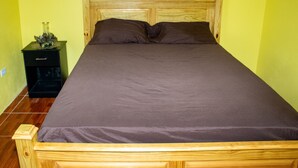 A wooden bed with a headboard, a dark brown bedspread, and a nightstand with a decorative item on it.
