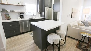 A modern kitchen with dark cabinets, a white countertop, and a built-in island with stools. - Mission Gorgeous - Complete Remodel (Scottsdale)