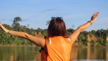 Una persona con una camisa naranja, con los brazos extendidos, mirando un cuerpo de agua y árboles al fondo.