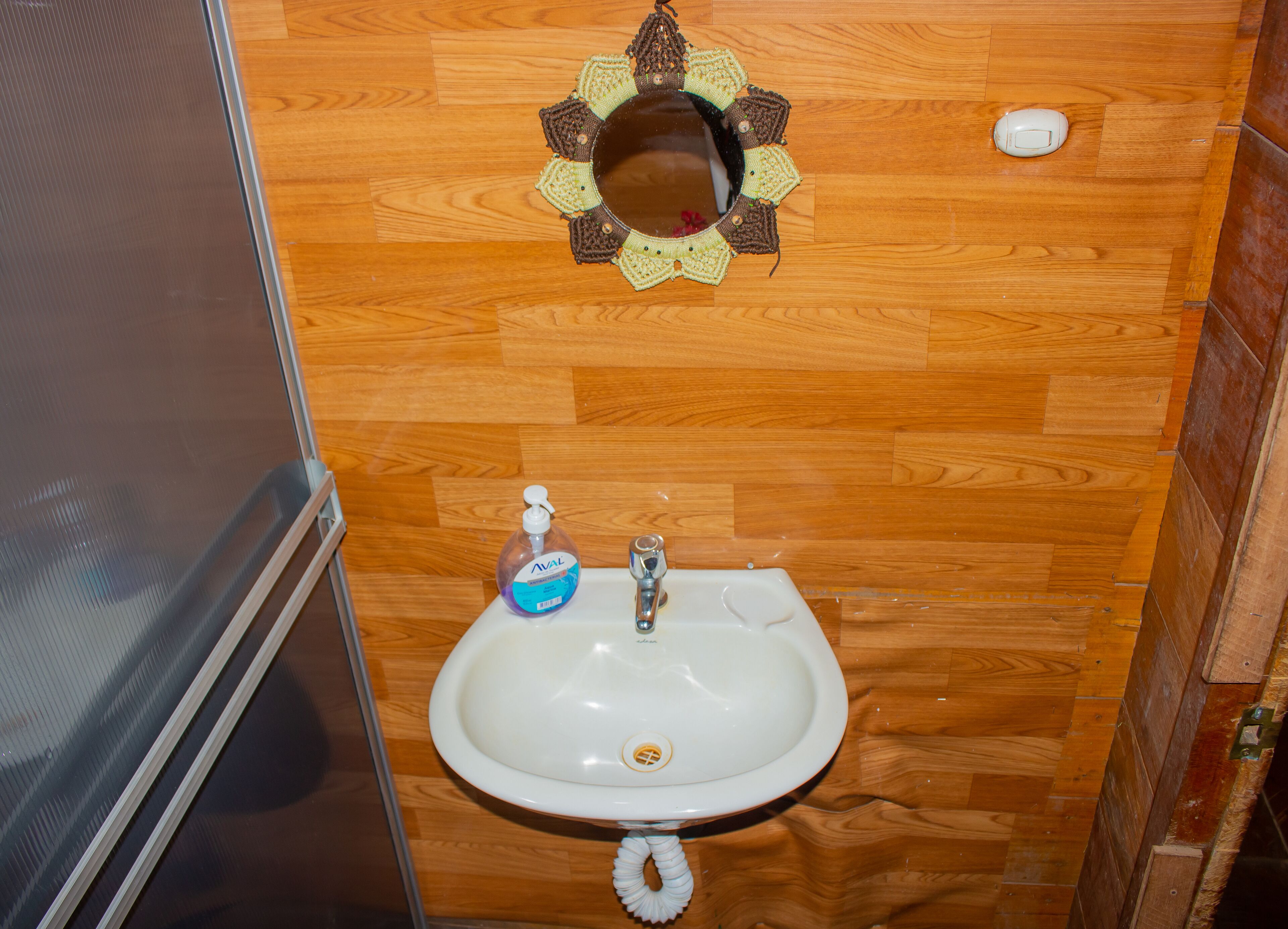 Ein Badezimmer mit Holzboden, einem weißen Waschbecken mit Seifenspender und einem dekorativen Spiegel darüber.
