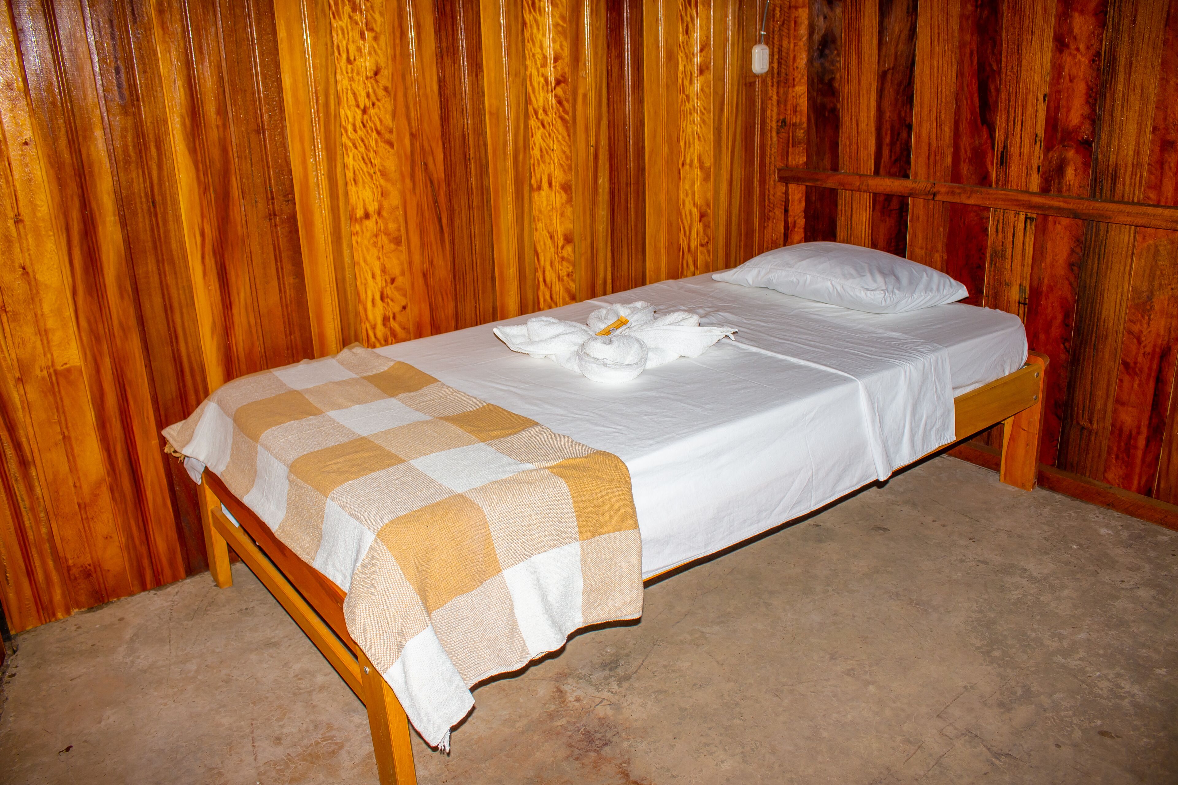 A single bed with a checkered blanket and white linens, set against a wooden wall.