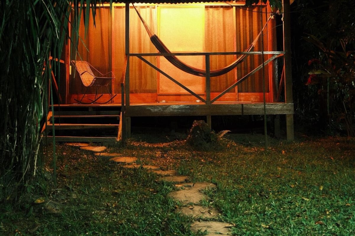A cozy, enclosed structure with a hammock, a wooden bench, and a small table, surrounded by lush greenery.