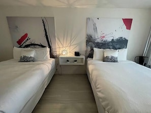 Une chambre d’hôtel avec deux lits, une table de chevet et des œuvres d’art abstraites accrochées au mur.