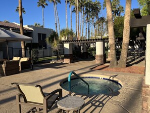 A pool area with lounge chairs and a table, surrounded by palm trees and a gated entrance.
