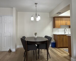 Un coin repas comprenant une table ronde, six chaises, un vase de fleurs et un lustre.