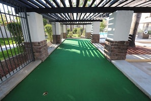 A covered walkway with artificial green turf, stone pillars, and metal railings.