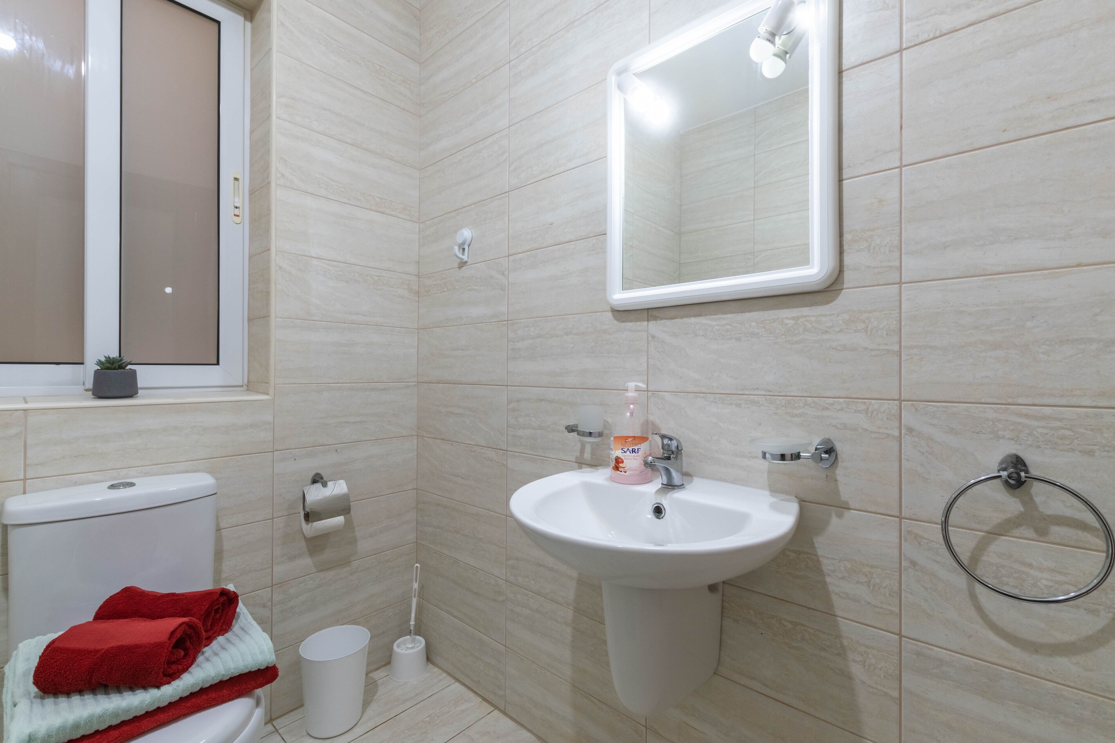 A bathroom with a toilet, sink, mirror, and towel rack.