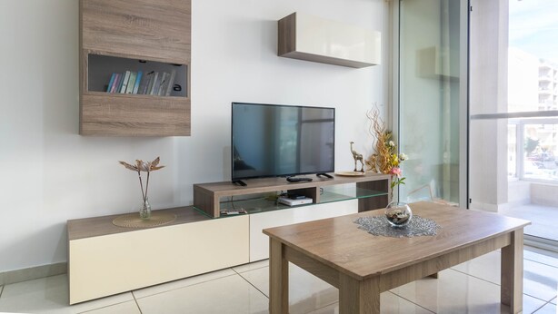 Una sala de estar moderna con un televisor de pantalla plana, una mesa de centro de madera y una mesa de comedor con superficie de vidrio.