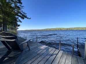 Eine Holzsteganlage mit einem Stuhl, mit Blick auf einen ruhigen See mit Booten und einer bewaldeten Uferlinie.