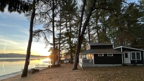 A cabin by a lake with a dock, surrounded by trees.