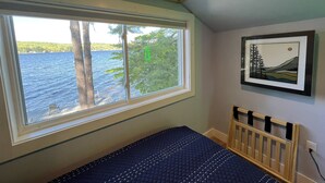 A room with a large window overlooking a body of water, a bed with a quilted cover, a wooden headboard, and a framed picture on the wall.