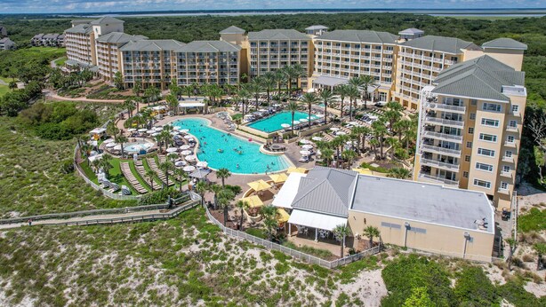 Lomakeskus, jossa on useita rakennuksia, keskeisellä paikalla sijaitseva uima-allas ja vehreää kasvillisuutta ympärillä.