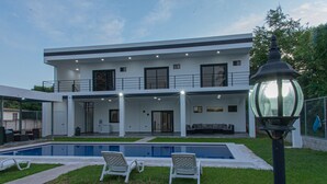 A modern two-story house with a swimming pool, outdoor seating, and a well-lit balcony. - Luxurious Villa with expansive room for family, couples/groups. 5 min beach walk (San Luis La Herradura)