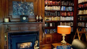 Une bibliothèque chaleureuse avec une cheminée, des étagères et une lampe décorative.