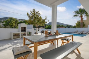 Une terrasse extérieure avec une table à manger, des bancs et une piscine.