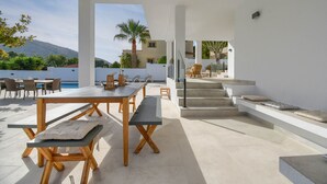 An outdoor patio area with a dining table, benches, and a pool view. - Graham Holiday Rentals - Magnolia (Moraira)