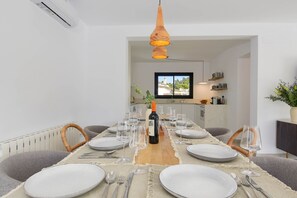 Un coin repas avec une longue table dressée pour six personnes, une bouteille de vin et des verres à vin vides.