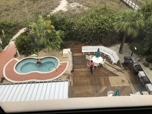 Un área de piscina con una pileta pequeña, una terraza de madera y una zona de estar con bancos blancos y una mesa.
