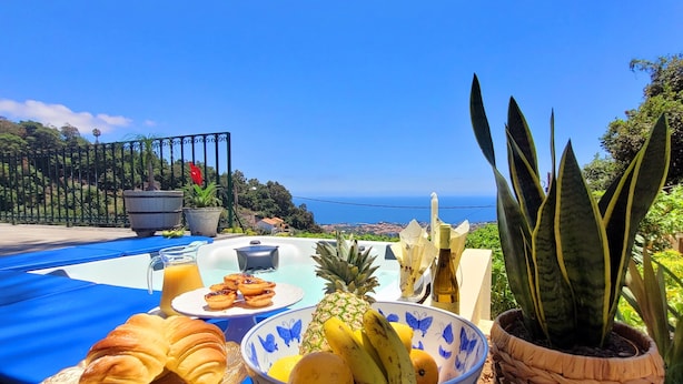 A breakfast table with croissants, pineapple, bananas, oranges, and juice, set against a scenic ocean view. - Quinta Martin, spacious villa with views of Funchal and the Atlantic Ocean  (Funchal)