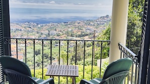 A balcony with two chairs and a table, overlooking a cityscape with buildings and greenery. - Quinta Martin, spacious villa with views of Funchal and the Atlantic Ocean  (Funchal)