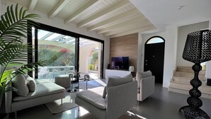 A modern living room with a sofa, armchairs, and a TV. There is a staircase leading to an upper level, and a large window offering a view of the outdoors. - Vacation home "Casa sulle colline di Barcuzzi" Pool, garden & barbecue (Barcuzzi)