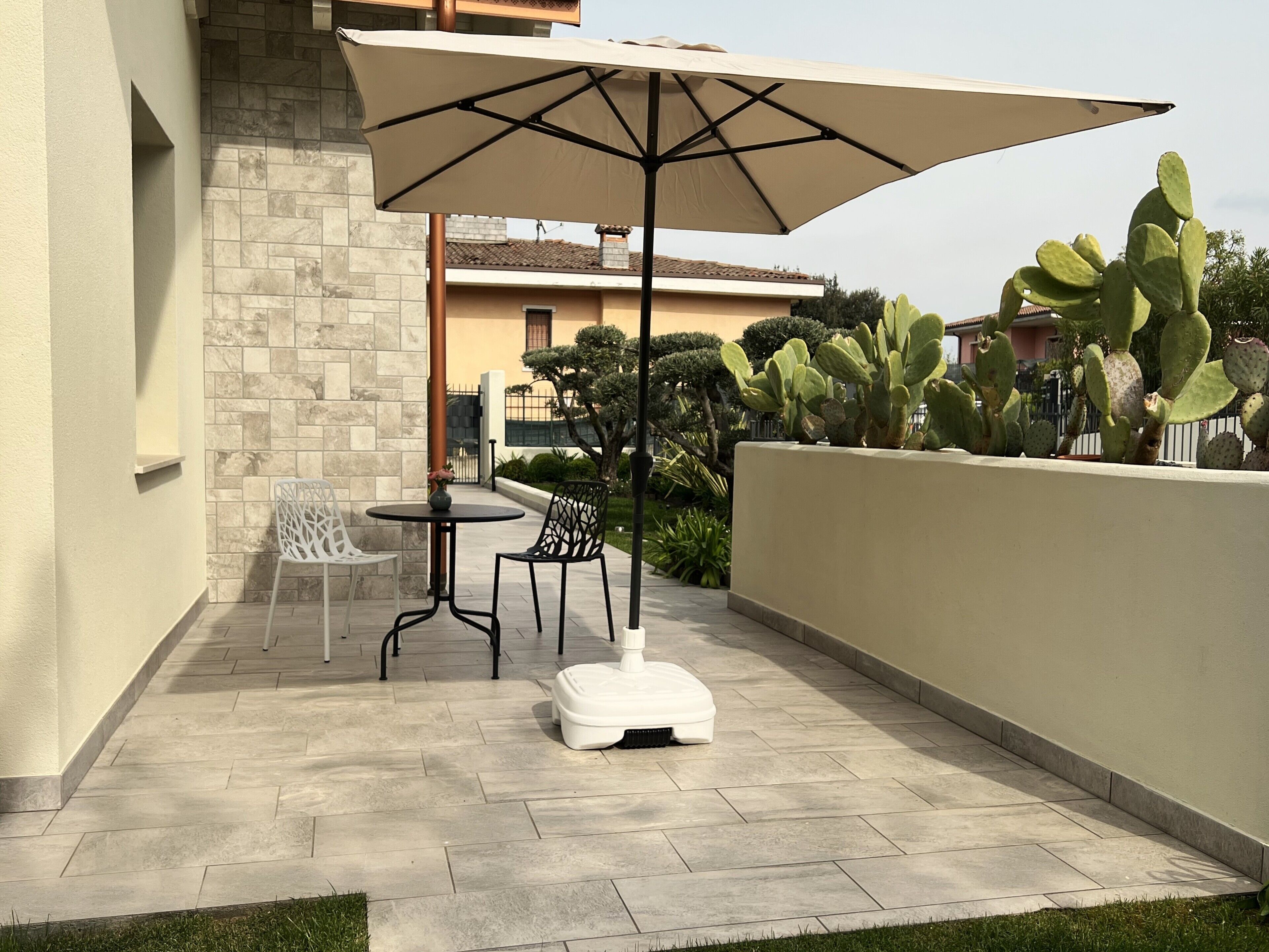 Une terrasse avec une table et des chaises, un grand parasol et un cactus.