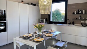 A modern kitchen with white cabinetry, a dining table set for two, and a large window providing a view of greenery outside. - Vacation home "Casa sulle colline di Barcuzzi" Pool, garden & barbecue (Barcuzzi)