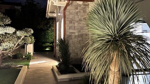 A modern house with a stone facade, a well-lit pathway, and a large palm tree. - Vacation home "Casa sulle colline di Barcuzzi" Pool, garden & barbecue (Barcuzzi)