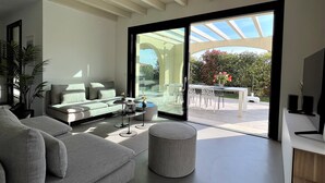 A modern living room with a grey sofa, a round ottoman, and a glass dining table with chairs. - Vacation home "Casa sulle colline di Barcuzzi" Pool, garden & barbecue (Barcuzzi)