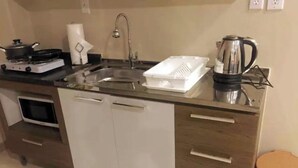 Una cocina compacta con estufa a gas, microondas, fregadero y hervidor.