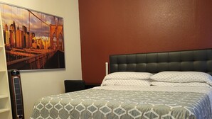 A bedroom with a bed, a headboard, a wall-mounted heater, a patterned rug, and a cityscape painting.