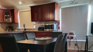A modern kitchen with dark wooden cabinets, a stainless steel microwave, and a dining area with a black table and chairs.