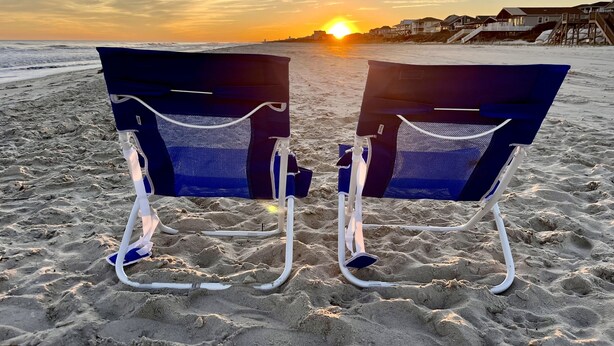 Deux chaises de plage sont placées face à l’océan, avec un coucher de soleil en arrière-plan.
