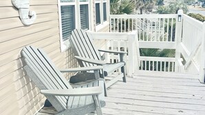 Une terrasse en bois avec deux fauteuils Adirondack, une clôture blanche en bois et une vue sur un quartier résidentiel.