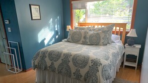 A bedroom with a bed, a nightstand, a window with blinds, and a door. - Spacious Home in Skagway Alaska (Skagway)