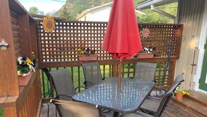 A wooden deck with a glass table and chairs, surrounded by a wooden fence with flower planters. - Spacious Home in Skagway Alaska (Skagway)