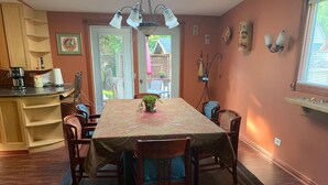 A dining area with a table covered in a patterned tablecloth, surrounded by wooden chairs. There is a potted plant on the table, and the room has wooden cabinets and a window with blinds. - Spacious Home in Skagway Alaska (Skagway)