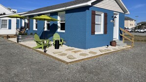 Ein blaues Haus mit überdachter Terrasse, Sitzgelegenheiten im Freien und einem kleinen Garten.