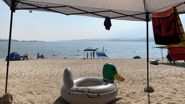 Une plage avec une tente, un matelas gonflable en forme de canard et une vue dégagée sur l’eau.