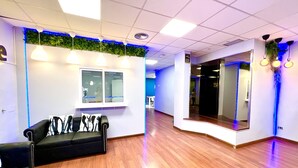 A reception area with a black leather sofa, a window with blinds, and a mirror with a black frame. - Hostel Thirty One (Madrid)