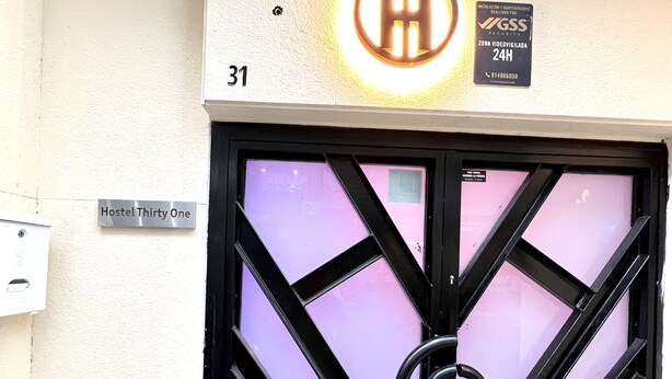 A building entrance with a black gate, a sign reading "Hostel Thirty One," and a security sign above the gate. - Hostel Thirty One (Madrid)