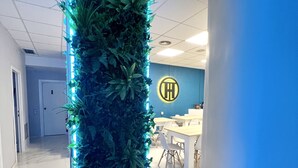 A hallway with a vertical garden illuminated by blue LED lights, a reception desk with a logo, and a dining area with tables and chairs. - Hostel Thirty One (Madrid)