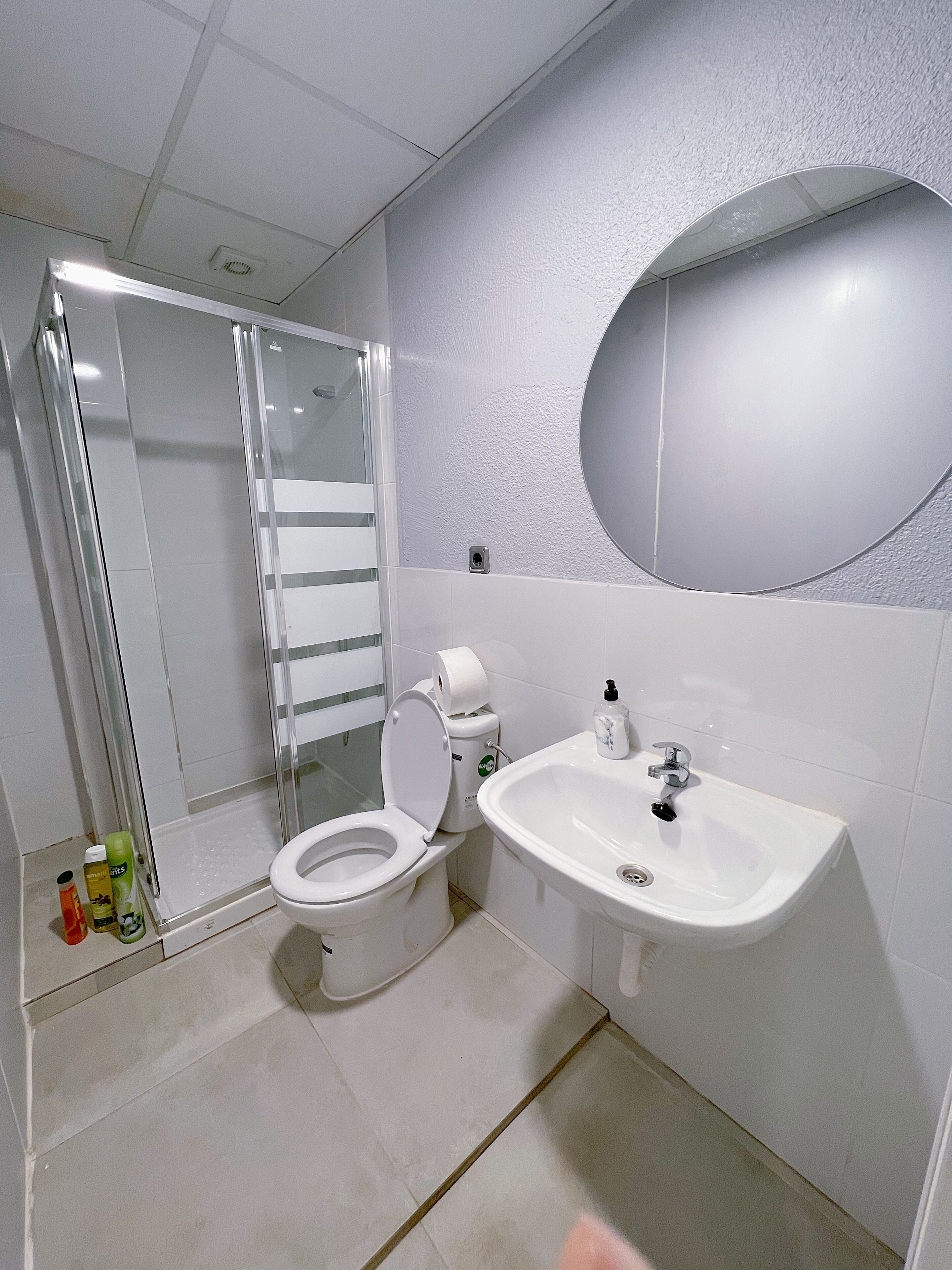 Et moderne badeværelse med brusekabine i glas, toilet, håndvask og spejl.