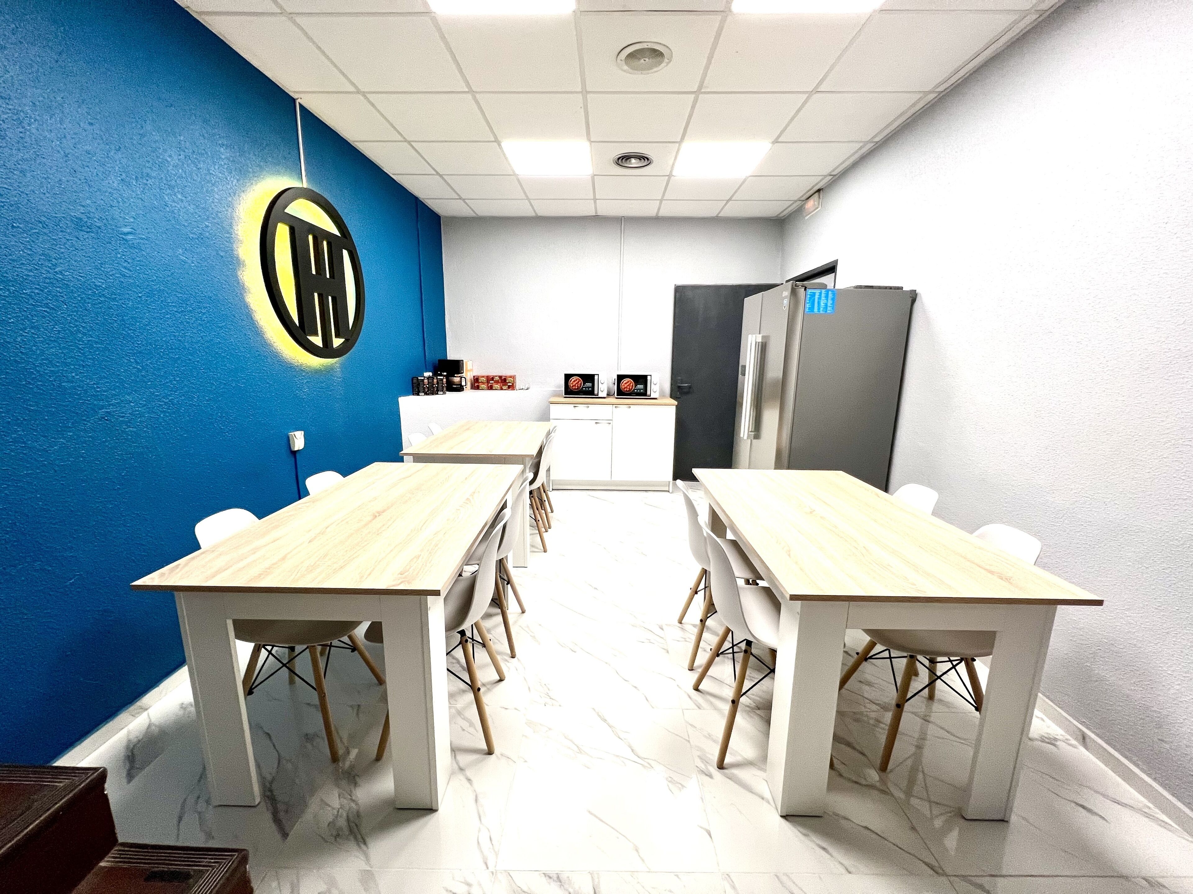 Un salón de conferencias con una pared azul decorativa, un logotipo, una kitchenette y un refrigerador.
