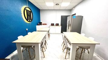 Un salón de conferencias con una pared azul decorativa, un logotipo, una kitchenette y un refrigerador.