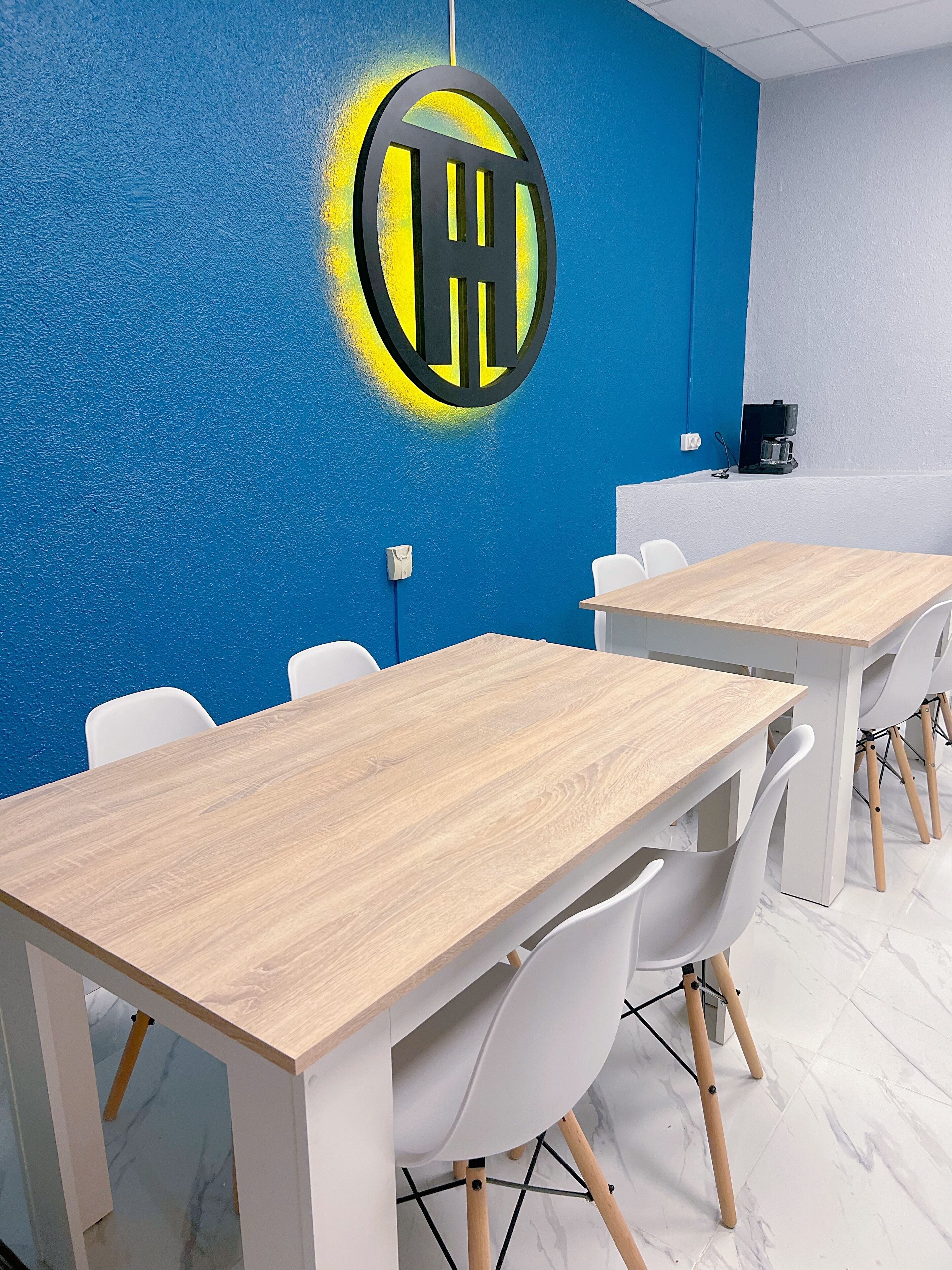 A modern meeting room with blue walls, a logo, white chairs, and wooden tables.